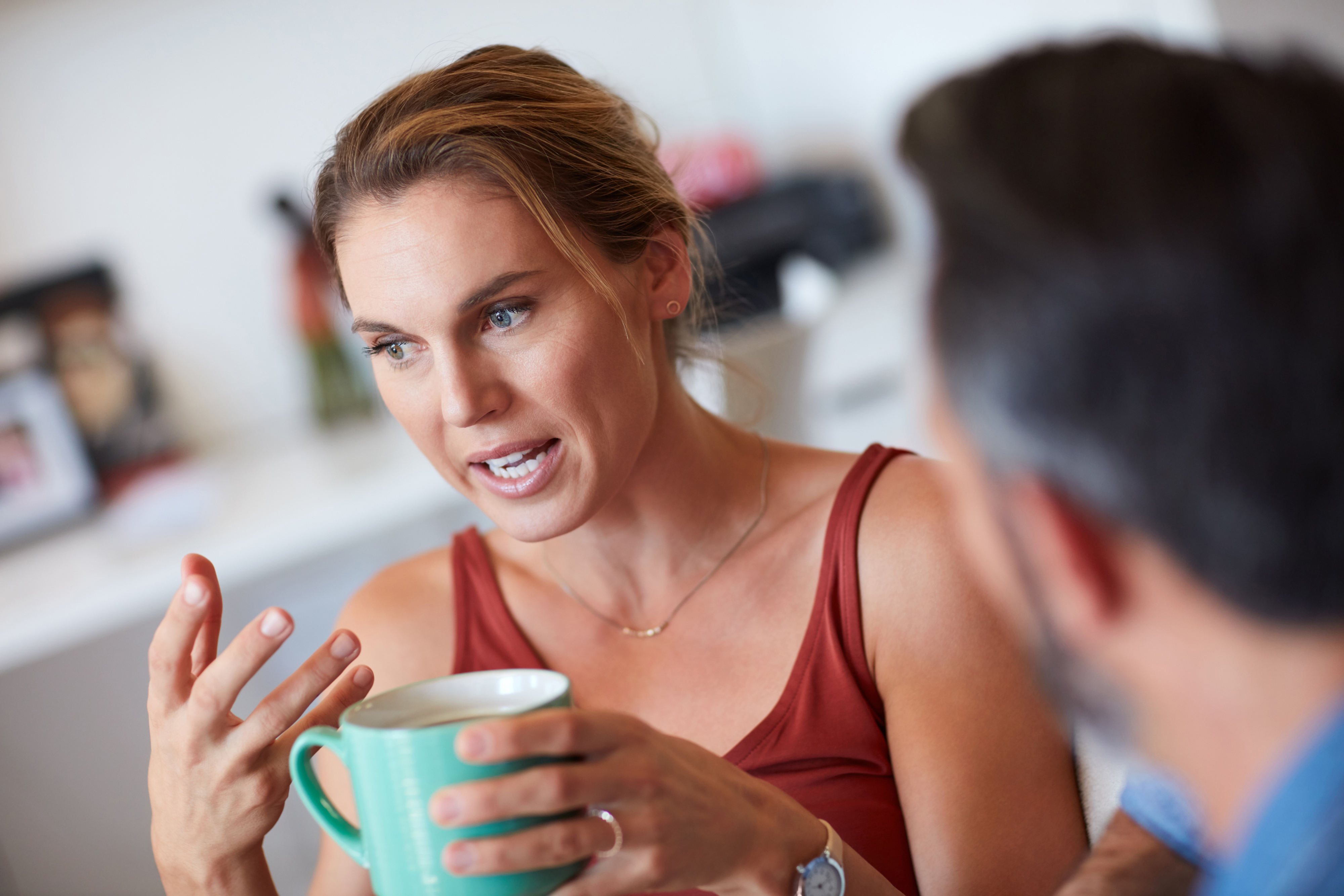 Woman holding a mug and talking to a man, both are casually dressed and indoors