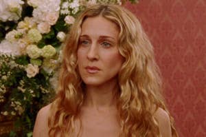 Carrie Bradshaw from Sex and the City, looking thoughtful, in a room with flowers in the background
