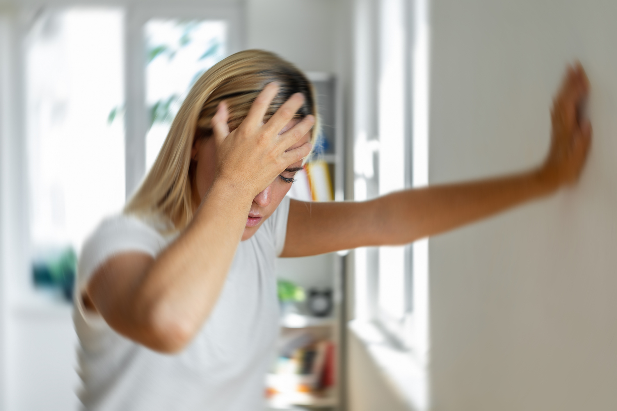 Person feeling dizzy with hand on forehead and one hand on wall for support