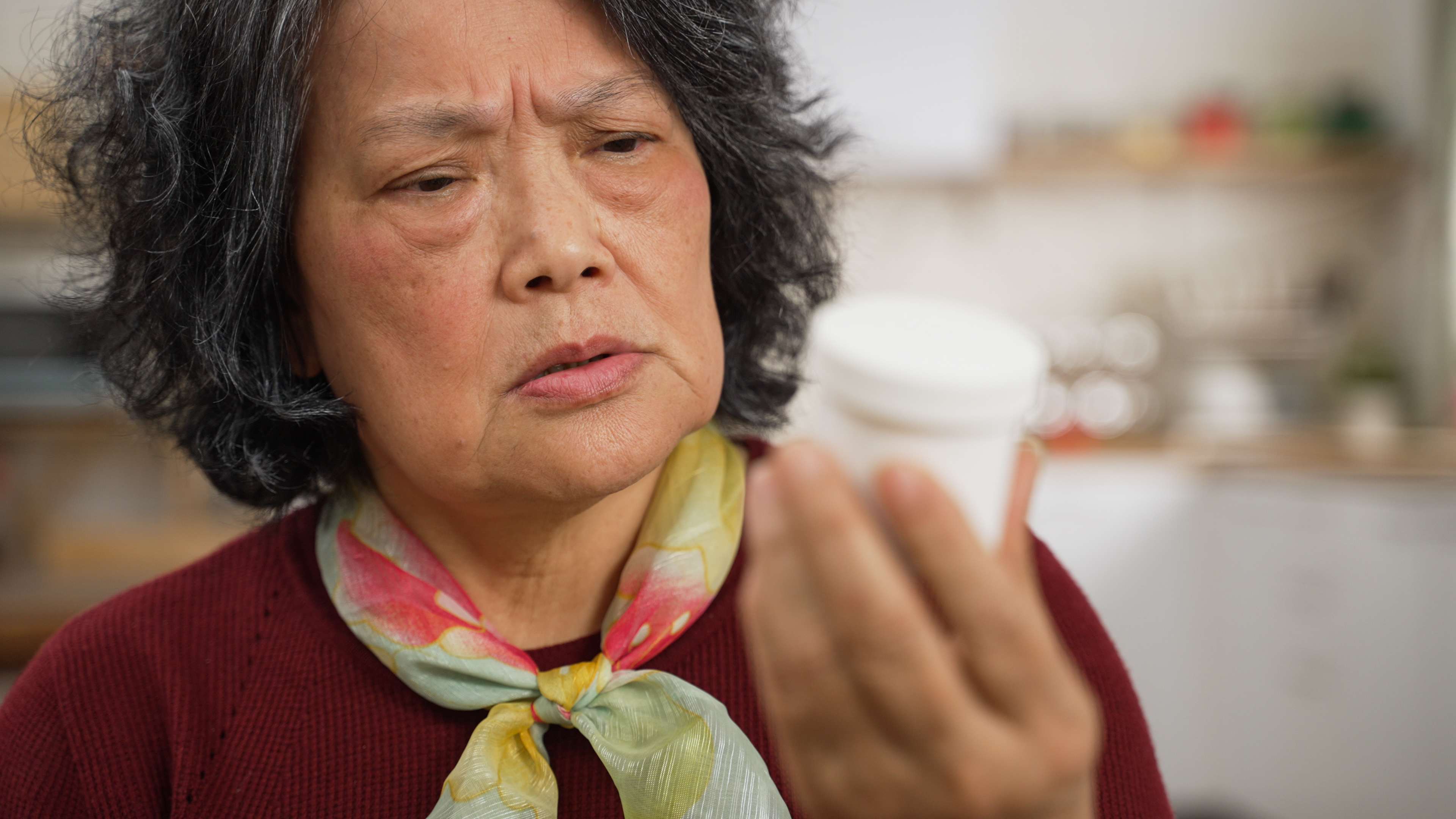 Woman frowning at a prescription bottle in her hand, appearing concerned or confused
