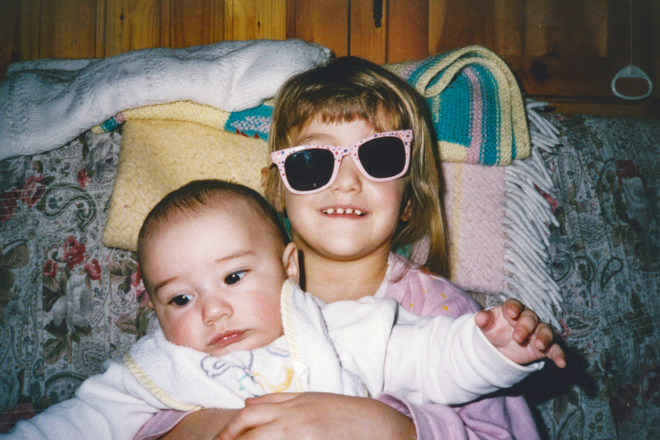 A vintage picture of two young children embracing, one wearing heart-shaped sunglasses, in a warm sibling moment