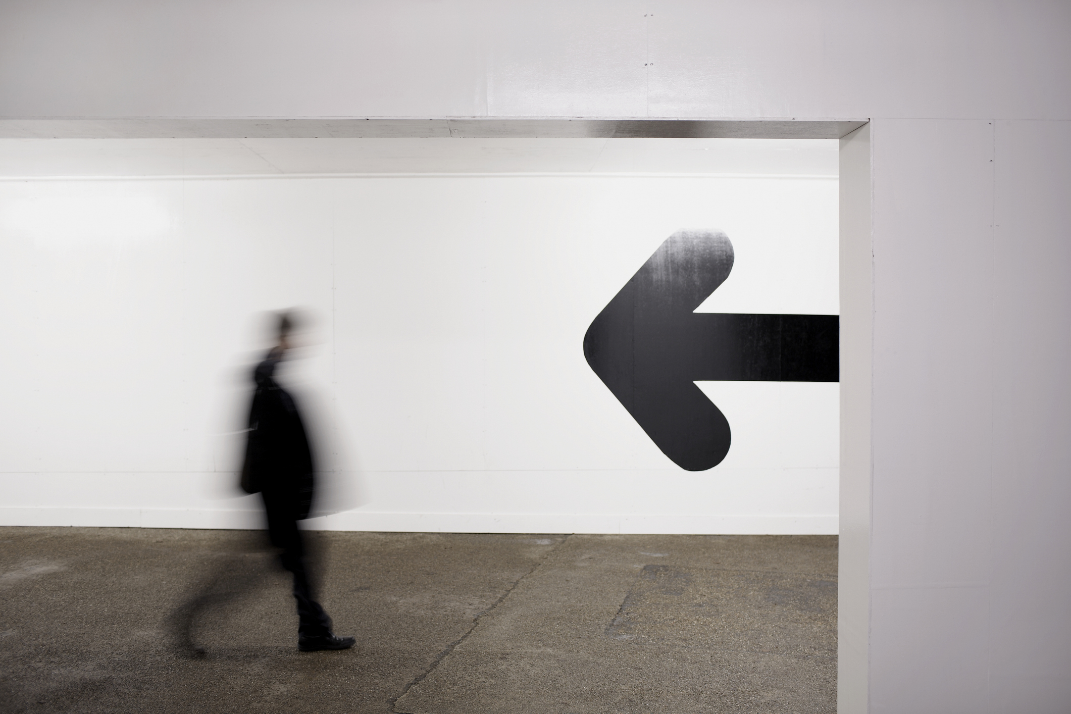 Person walking past a large arrow pointing left on a wall