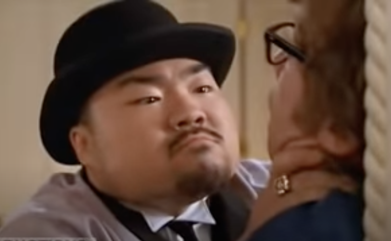 Joe Son in hat with an angry expression staring at Austin Powers whose back faces the camera