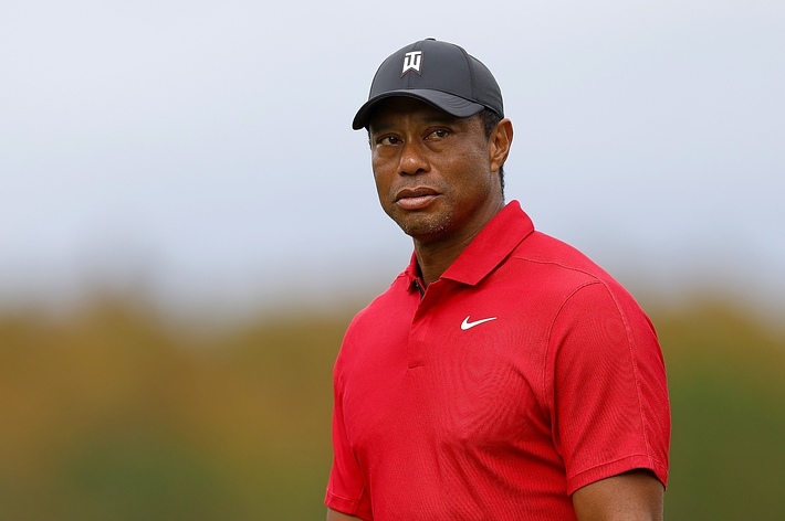 Tiger Woods wearing a red shirt and cap, staring into the distance on a golf course