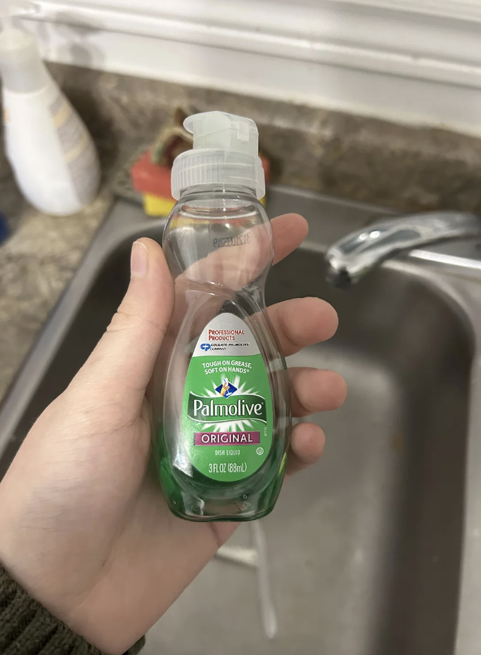 Person holding a tiny Palmolive dish soap bottle over a sink