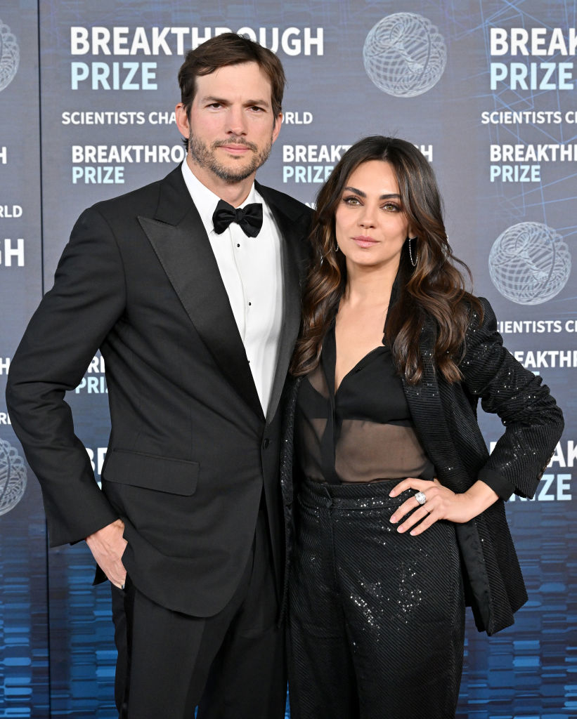 Two individuals at an event, one in a black tuxedo and the other in a sparkling outfit with a sheer overlay