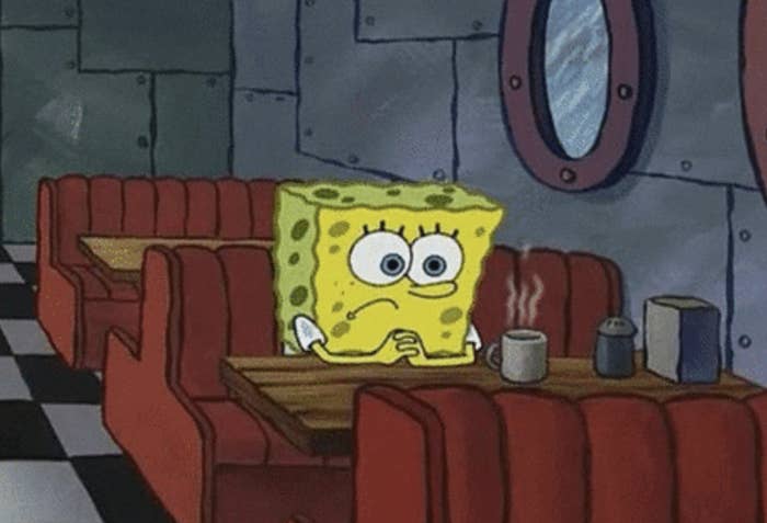 SpongeBob SquarePants sitting at a table looking tired with a coffee cup in front of him