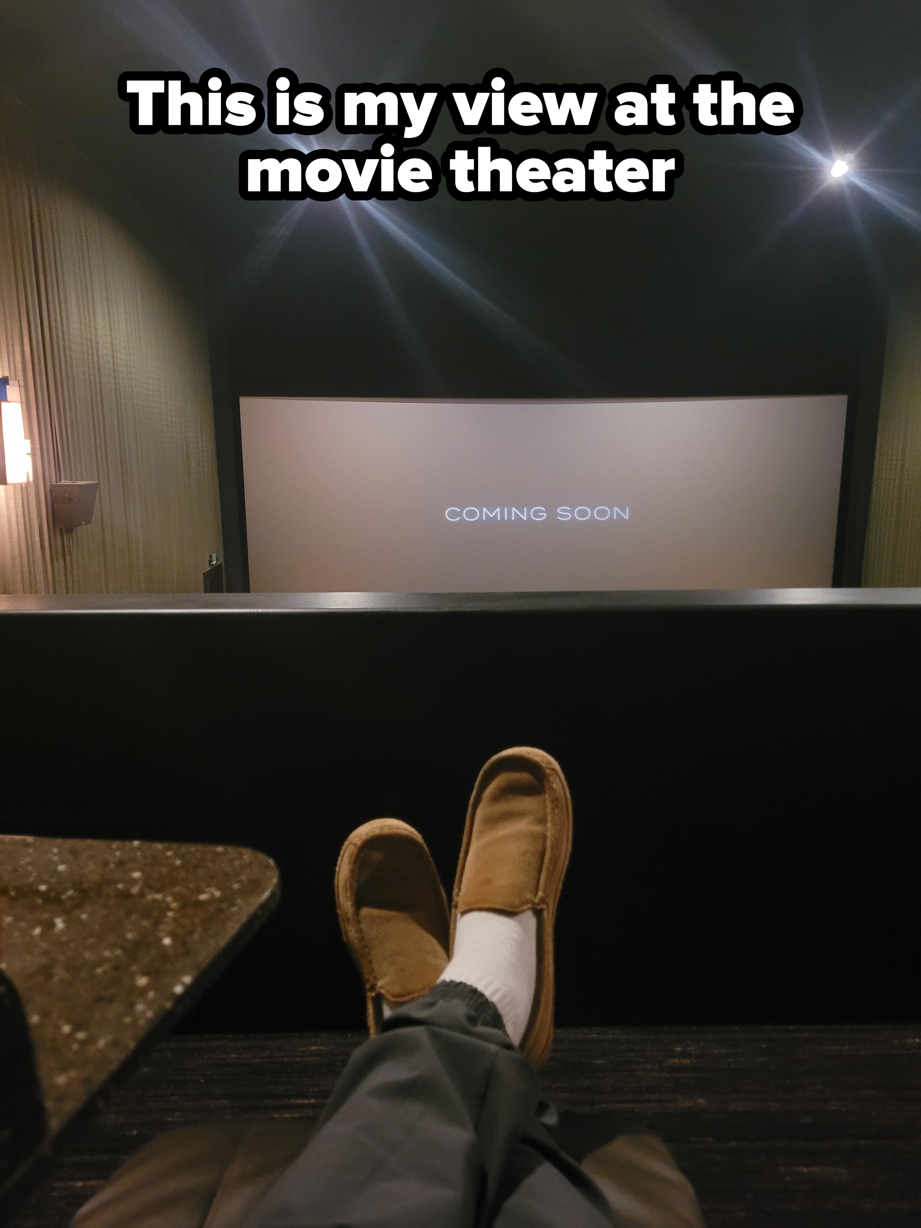 Person in a theater with feet on railing, &quot;COMING SOON&quot; on screen