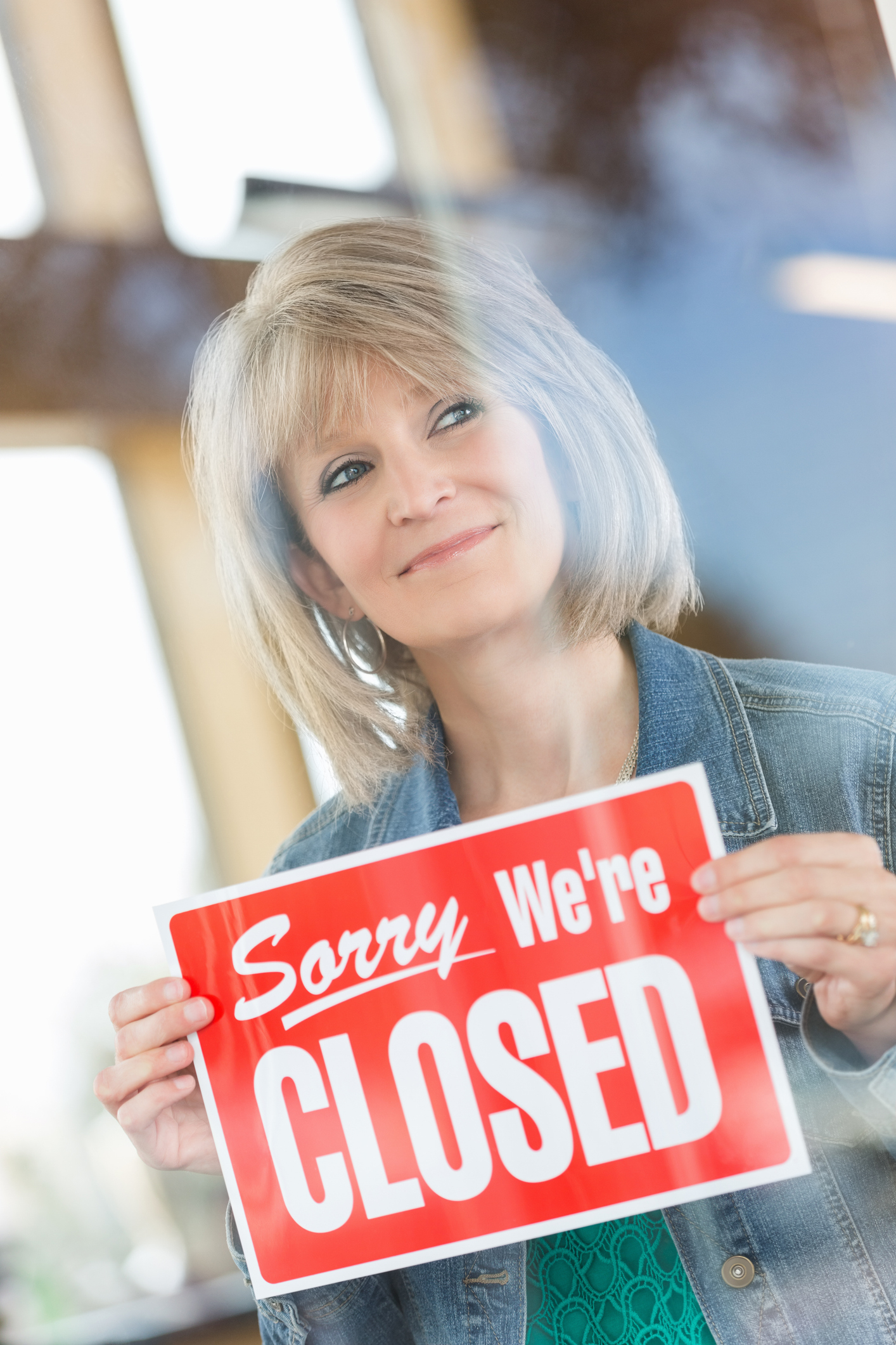 Woman holding a &#x27;Sorry We&#x27;re Closed&#x27; sign, viewed through a glass pane