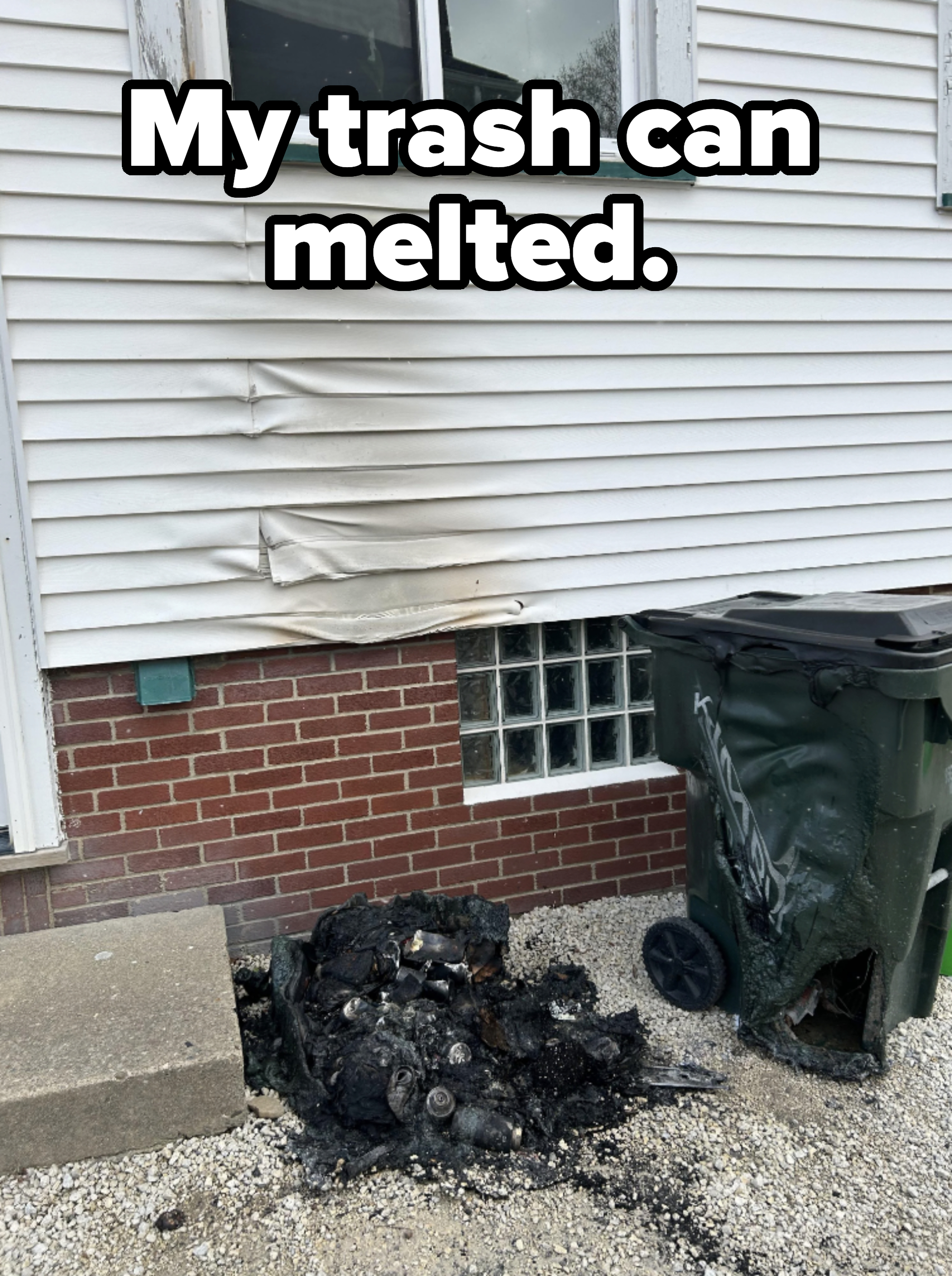 Melted siding on a house next to a burned trash bin with debris