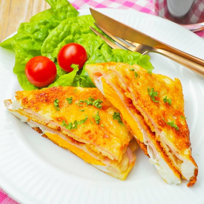 ハムとチーズが挟まれた料理が皿に盛られ、横にレタスとトマトが添えられています。