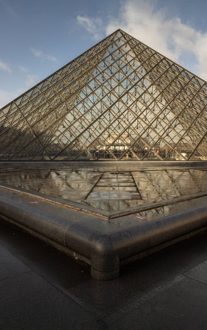 Pirámide de vidrio del Louvre con cielo despejado y reflejo en agua