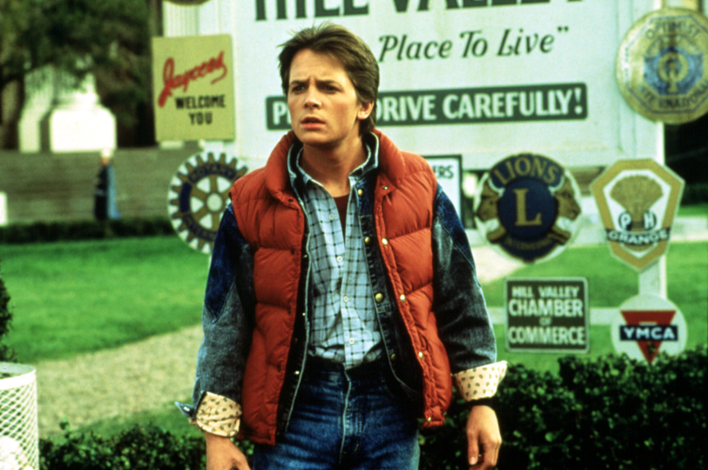 Marty McFly from Back to the Future stands confused in front of a "Welcome to Hill Valley" sign, wearing a denim jacket