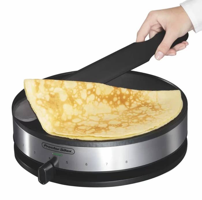 Hand flipping a crepe on an electric crepe maker