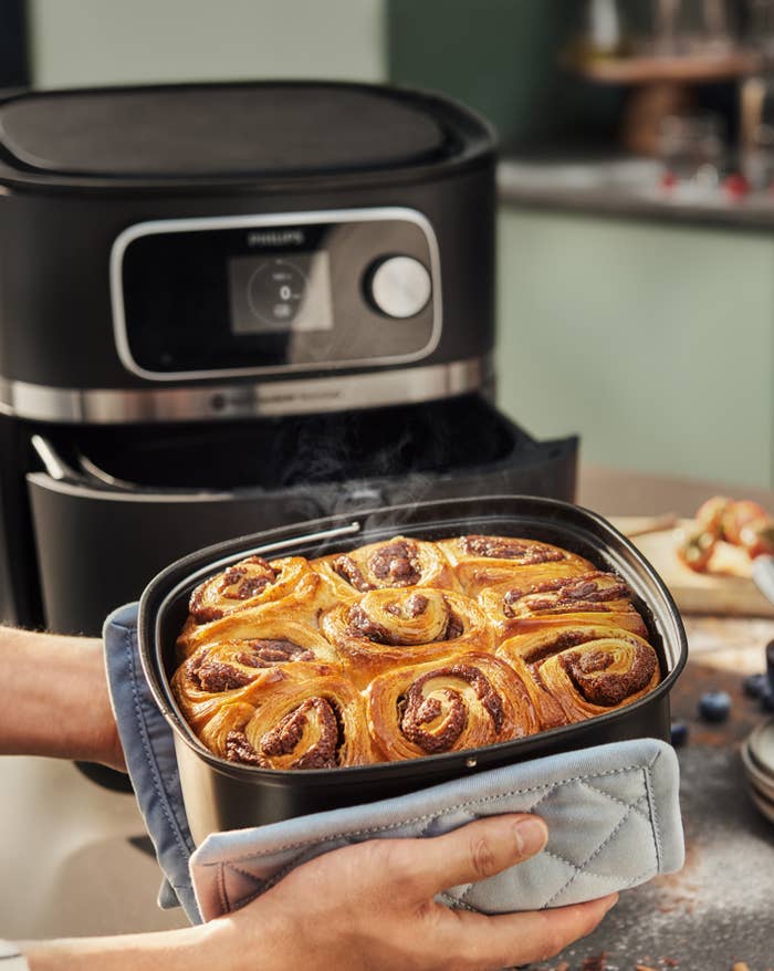Person holding a baking tray with freshly baked cinnamon rolls from an air fryer