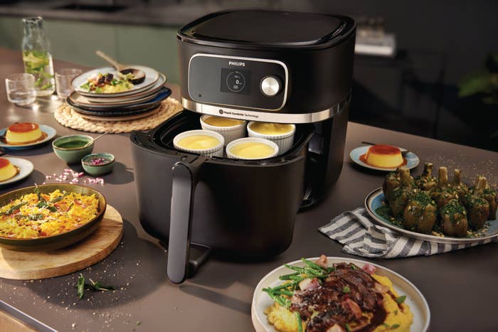 Philips air fryer on counter surrounded by various cooked dishes, illustrating its use in preparing meals