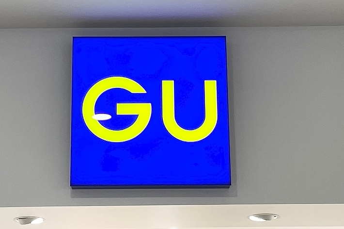 Sign with the letters &ldquo;GU&rdquo; on a blue background, mounted on a wall with ceiling lights