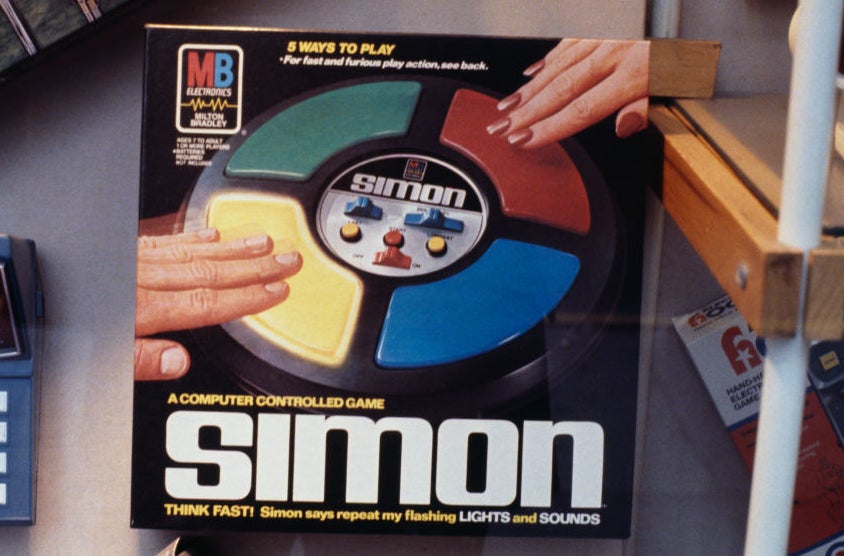 Person&#x27;s hands playing Simon, a classic electronic memory game with four colored buttons. Retro gaming nostalgia