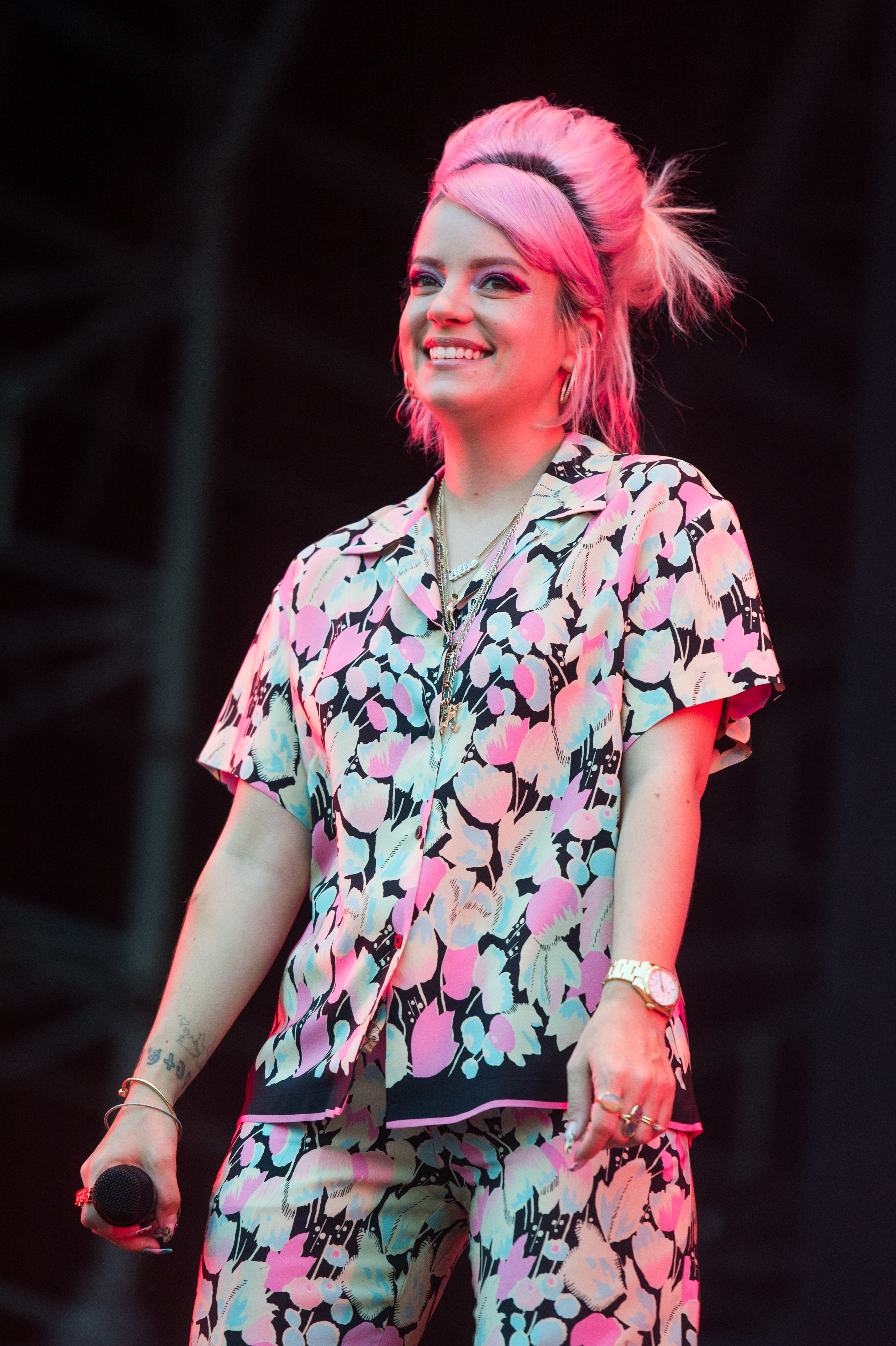 Lily Allen smiling on stage in a floral outfit with a microphone in hand