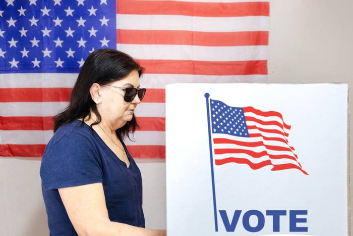 Woman standing next to a voting booth with an American flag design, about to cast a vote