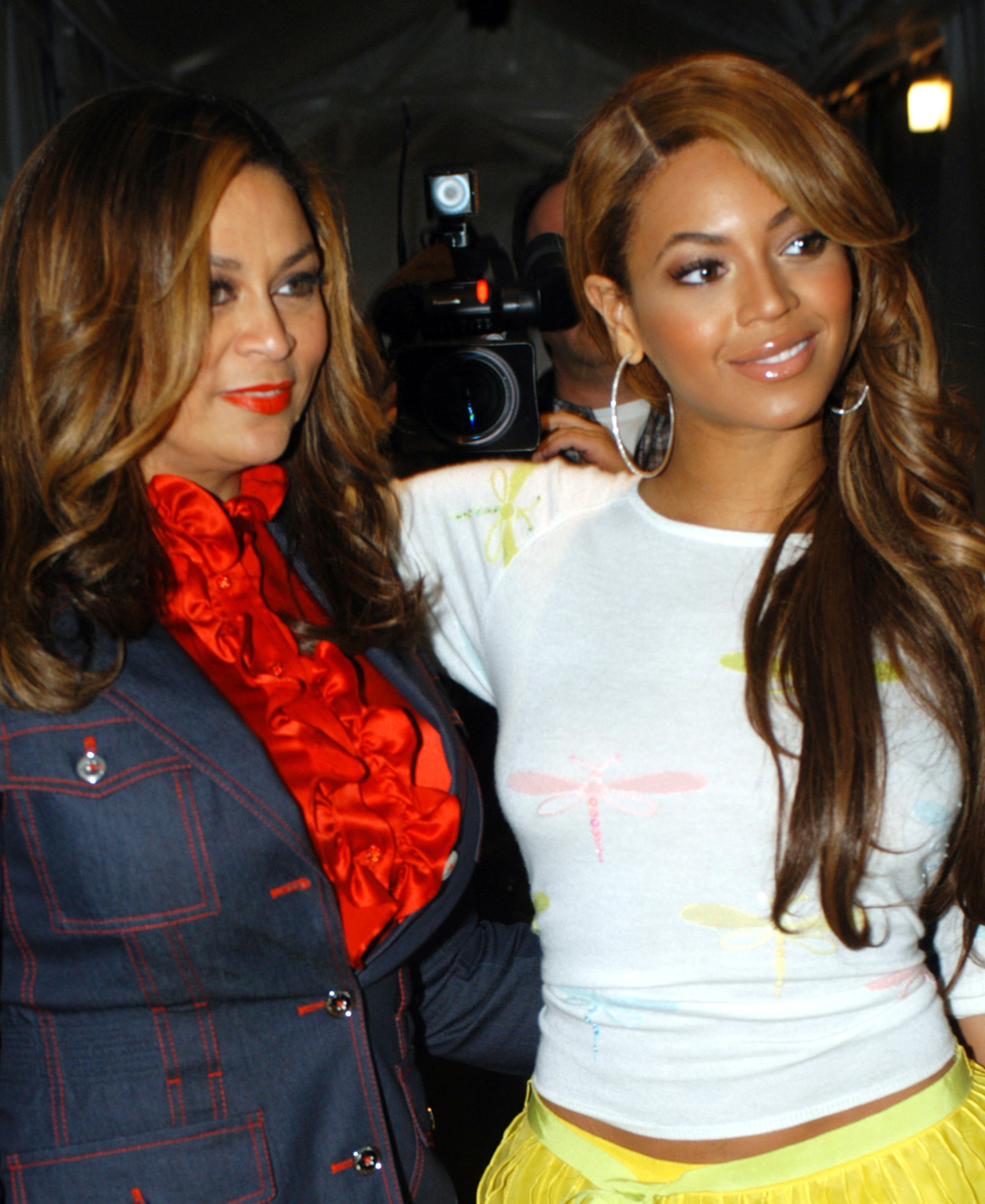 Tina Knowles and 叠别测辞苍肠é stand side by side, Tina in a denim jacket, 叠别测辞苍肠é in a graphic tee and yellow skirt