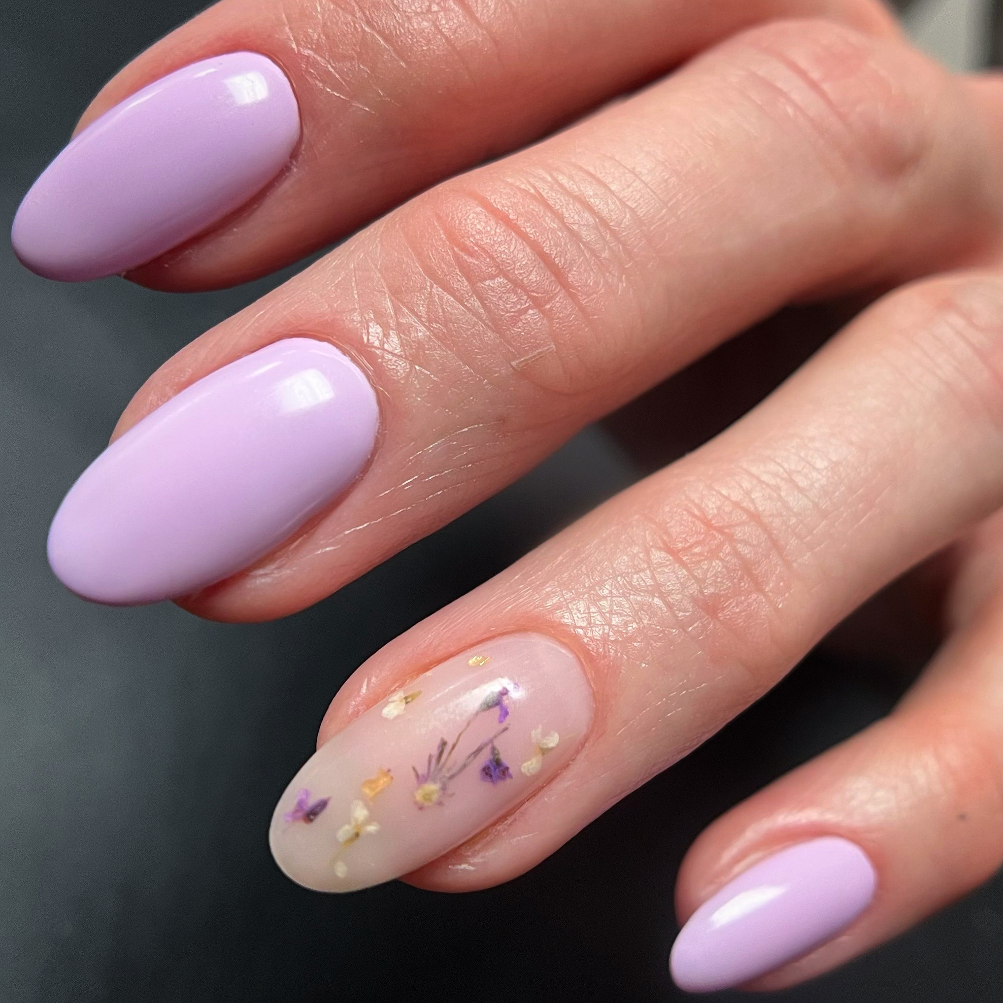 Close-up of a hand with purple manicured nails, one nail featuring a floral design