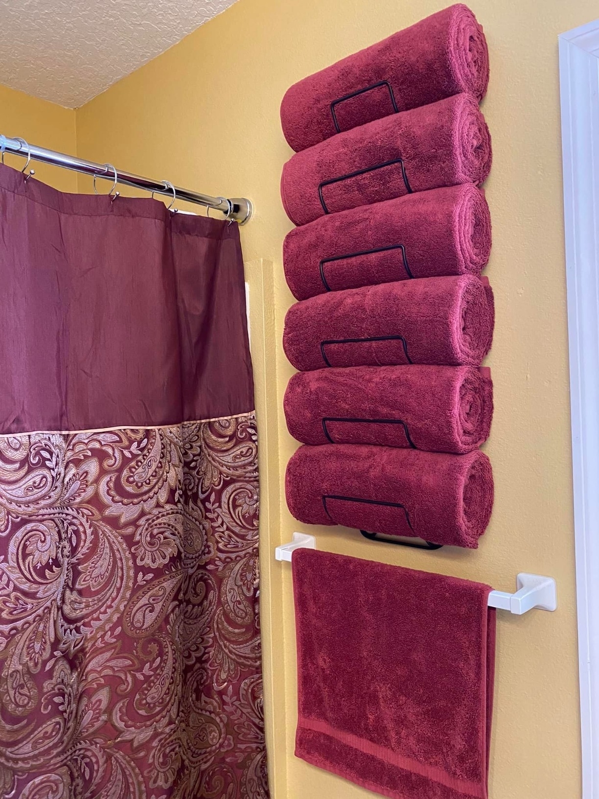 Five plush red towels neatly rolled and stacked on a wall-mounted shelf in a bathroom
