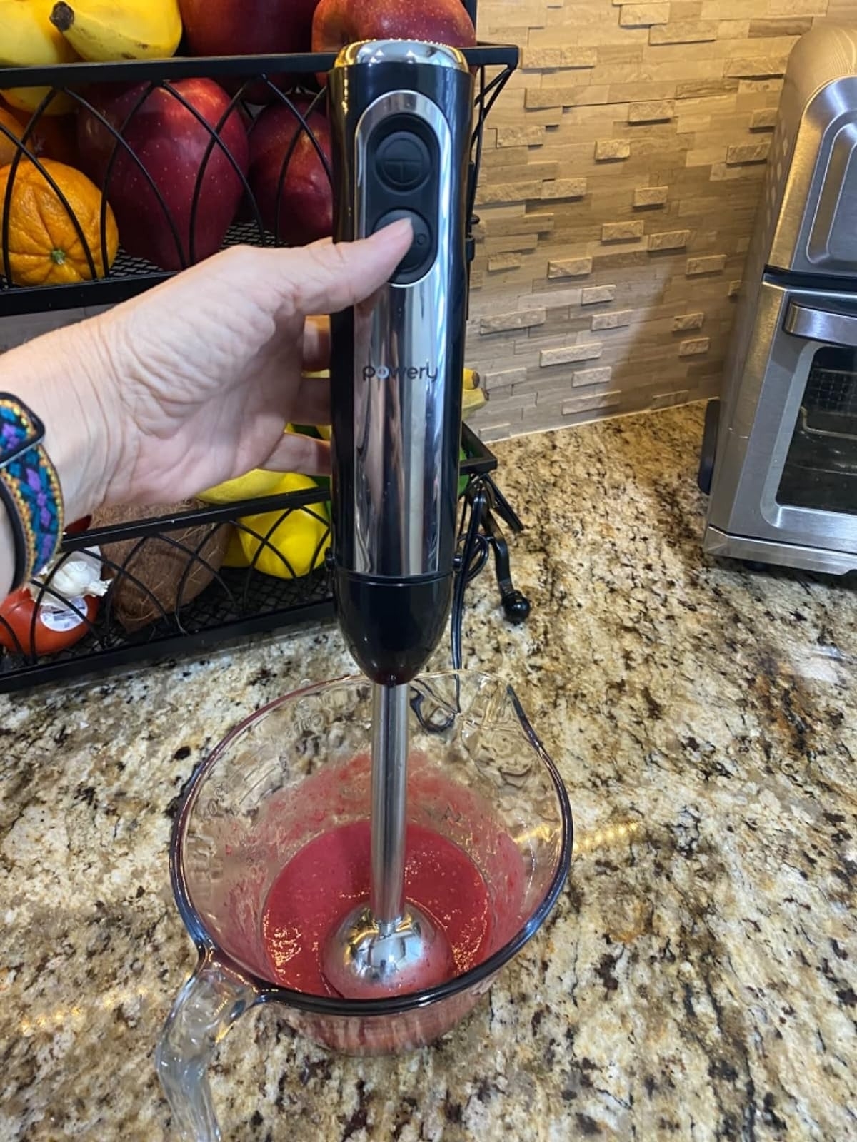 Person using a handheld immersion blender to mix ingredients in a glass bowl on a kitchen counter