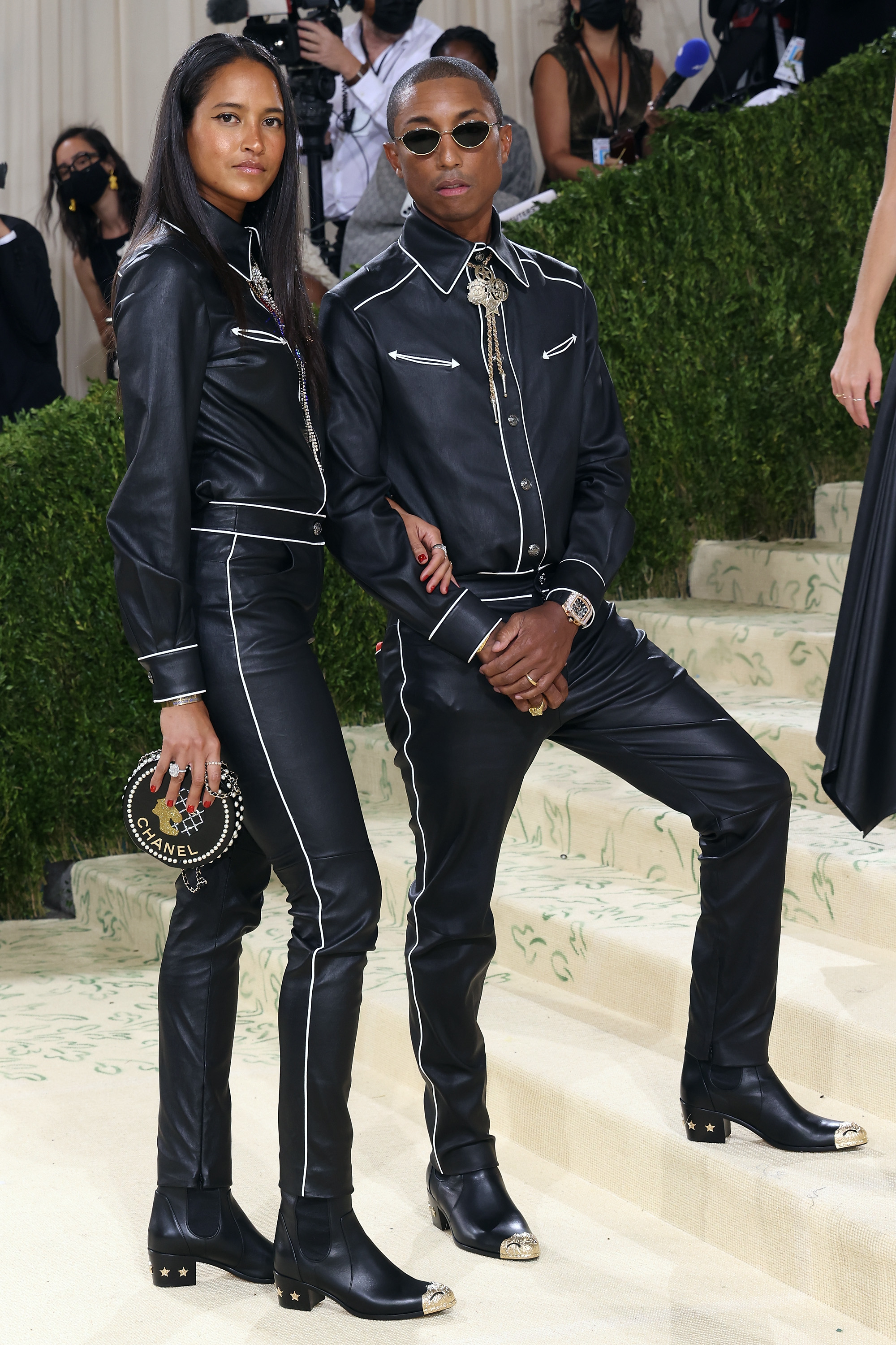 Two individuals at a themed event, dressed in matching black leather outfits with white accents, posing on stairs