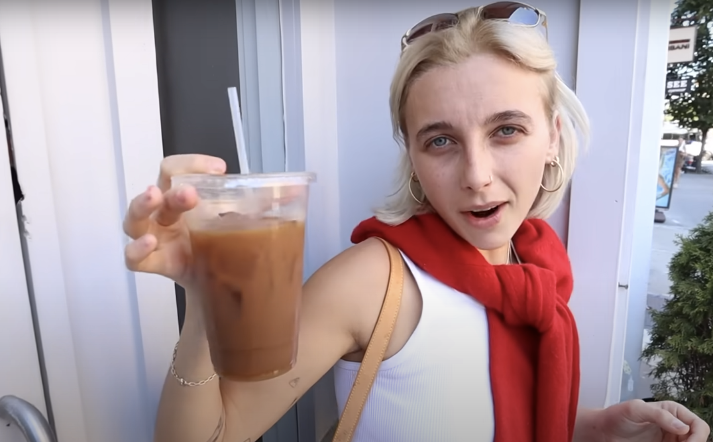 Woman holding iced coffee, wearing a white top, red scarf, and sunglasses on head