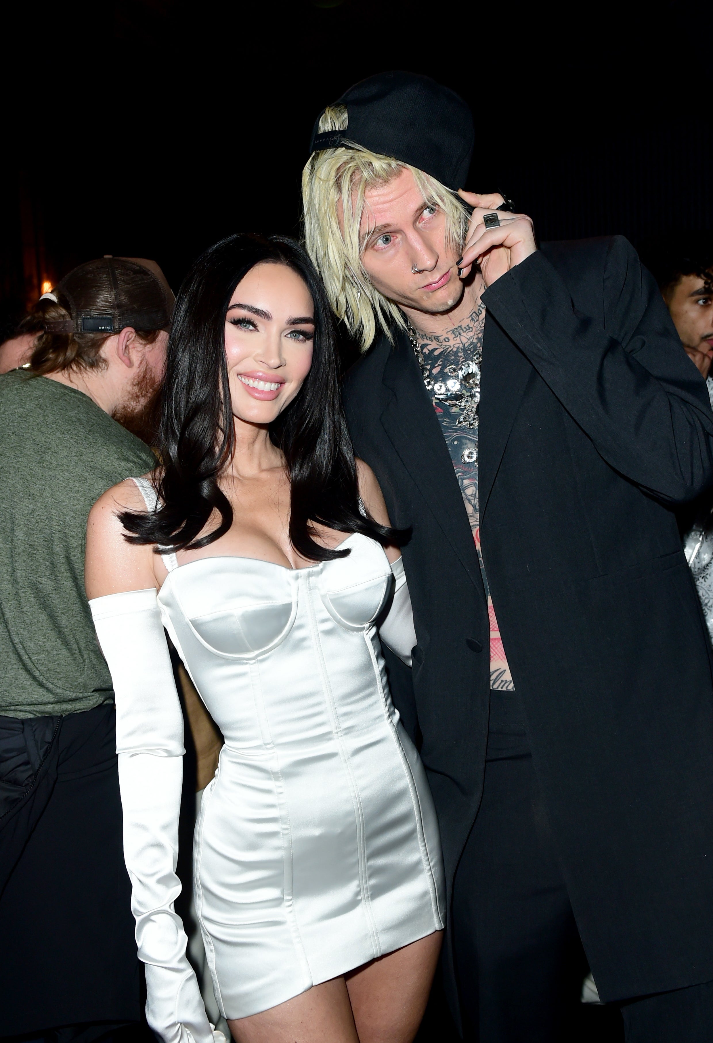 Megan Fox in a corset dress with gloves, and Machine Gun Kelly in a suit with silver chain necklaces at an event