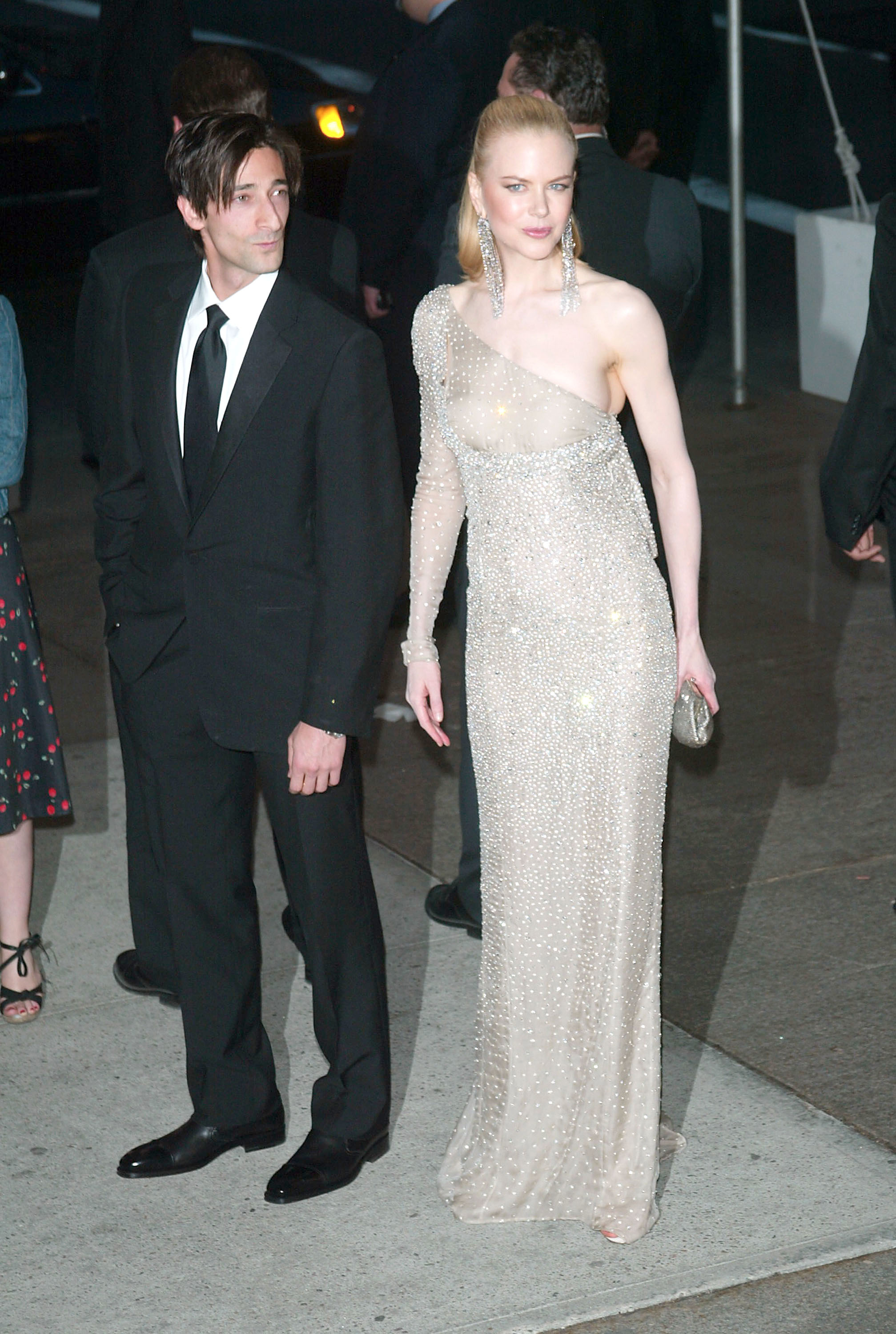 Two celebrities on the red carpet; the woman is in a beaded gown with a sheer overlay, the man in a classic black suit
