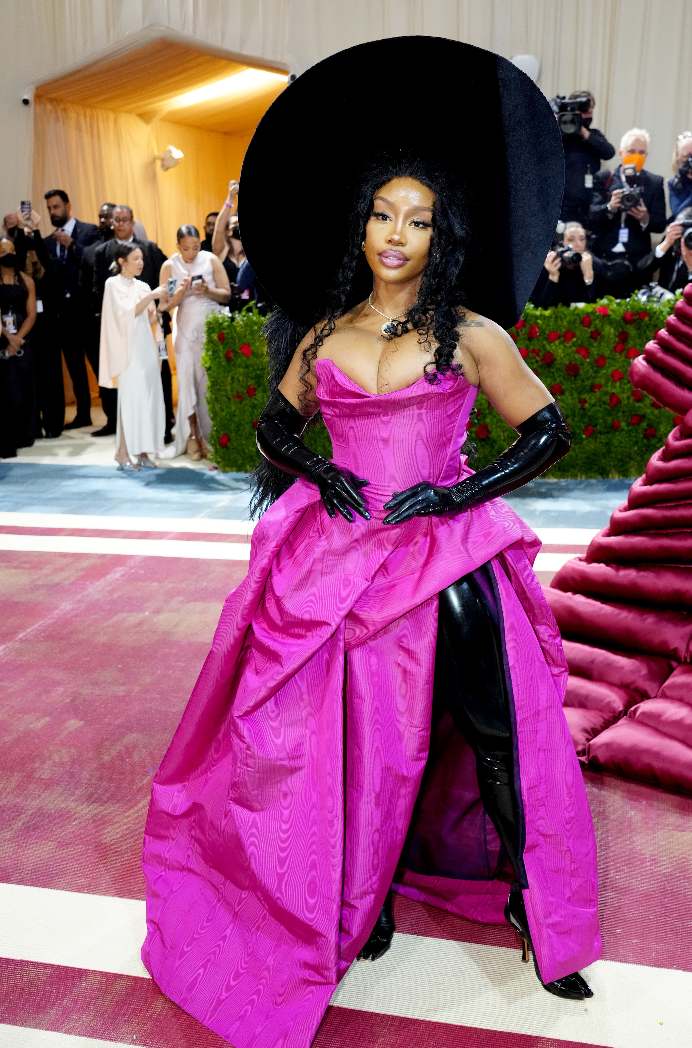 Woman in oversized black hat and pink gown with black gloves posing on stairs