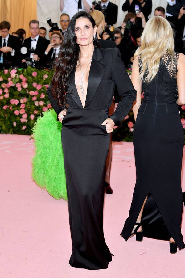 Demi Moore at an event in a black suit with a plunging neckline, accessorized with a green feathered bag