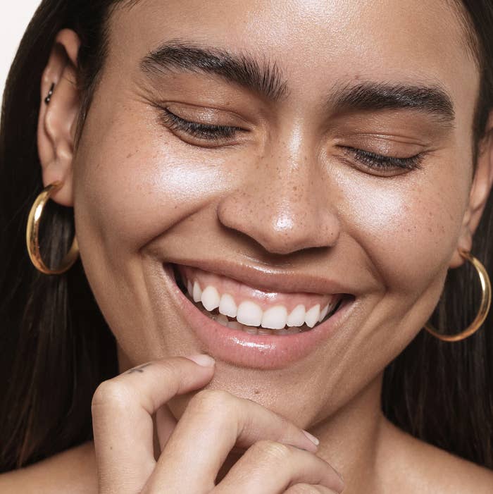 Person smiling with closed eyes, showing freckles, wearing hoop earrings