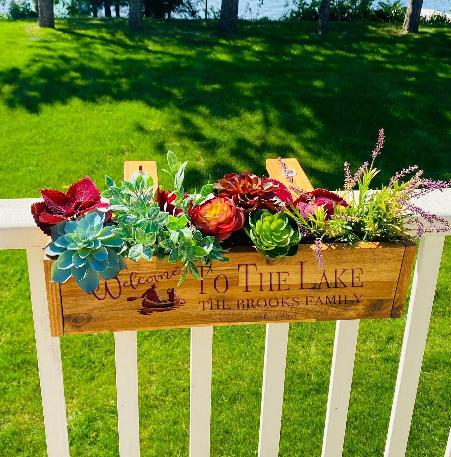 Plants and a personalized sign saying &#x27;Welcome to the Lake, The Brooks Family&#x27; on a fence with a lake in the background