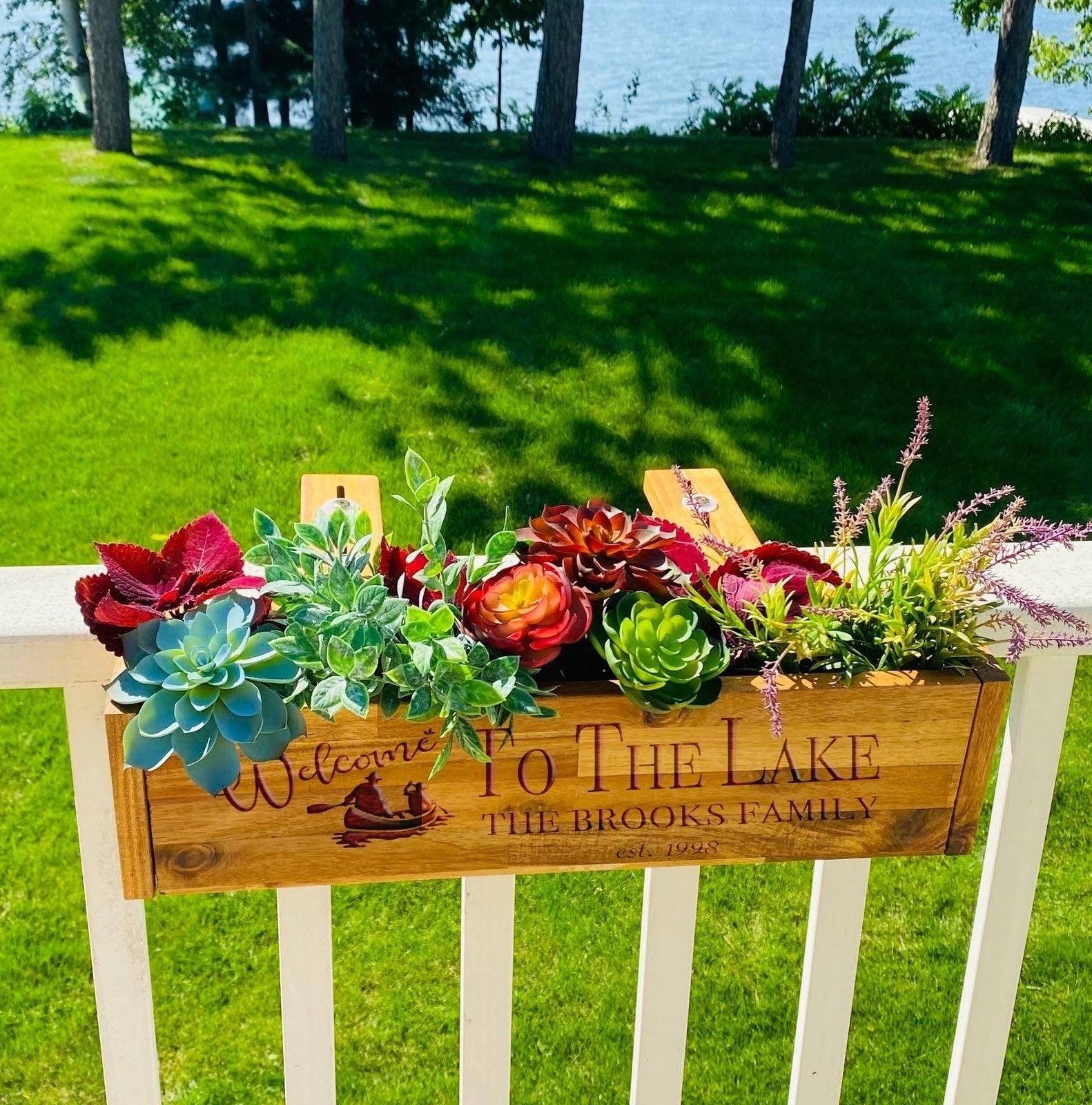 Plants and a personalized sign saying &#x27;Welcome to the Lake, The Brooks Family&#x27; on a fence with a lake in the background