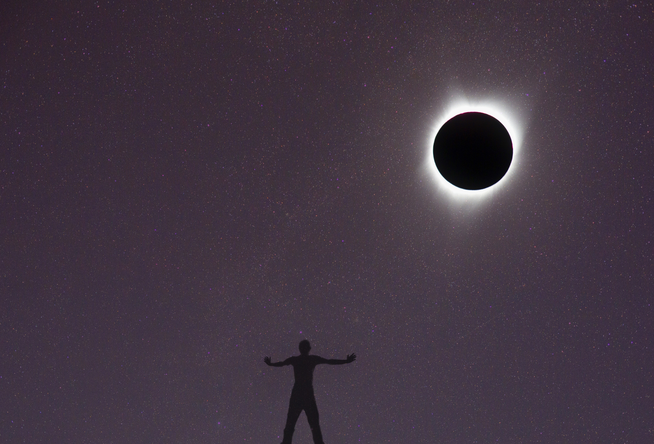 Silhouetted person with arms extended under a solar eclipse