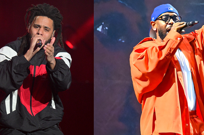 Two male artists perform onstage, one in a track jacket and the other in a red coat and cap