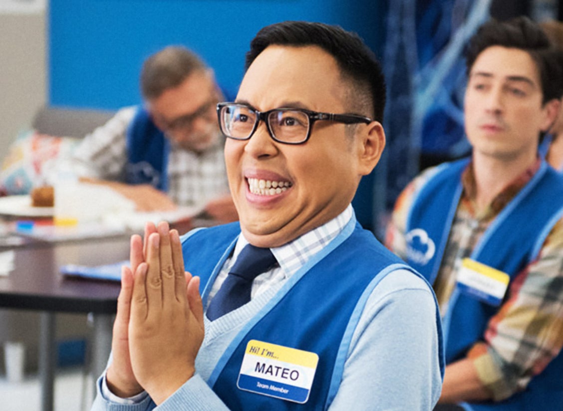Mateo from &quot;Superstore&quot; smiling and clapping, seated in the breakroom with co-workers behind him