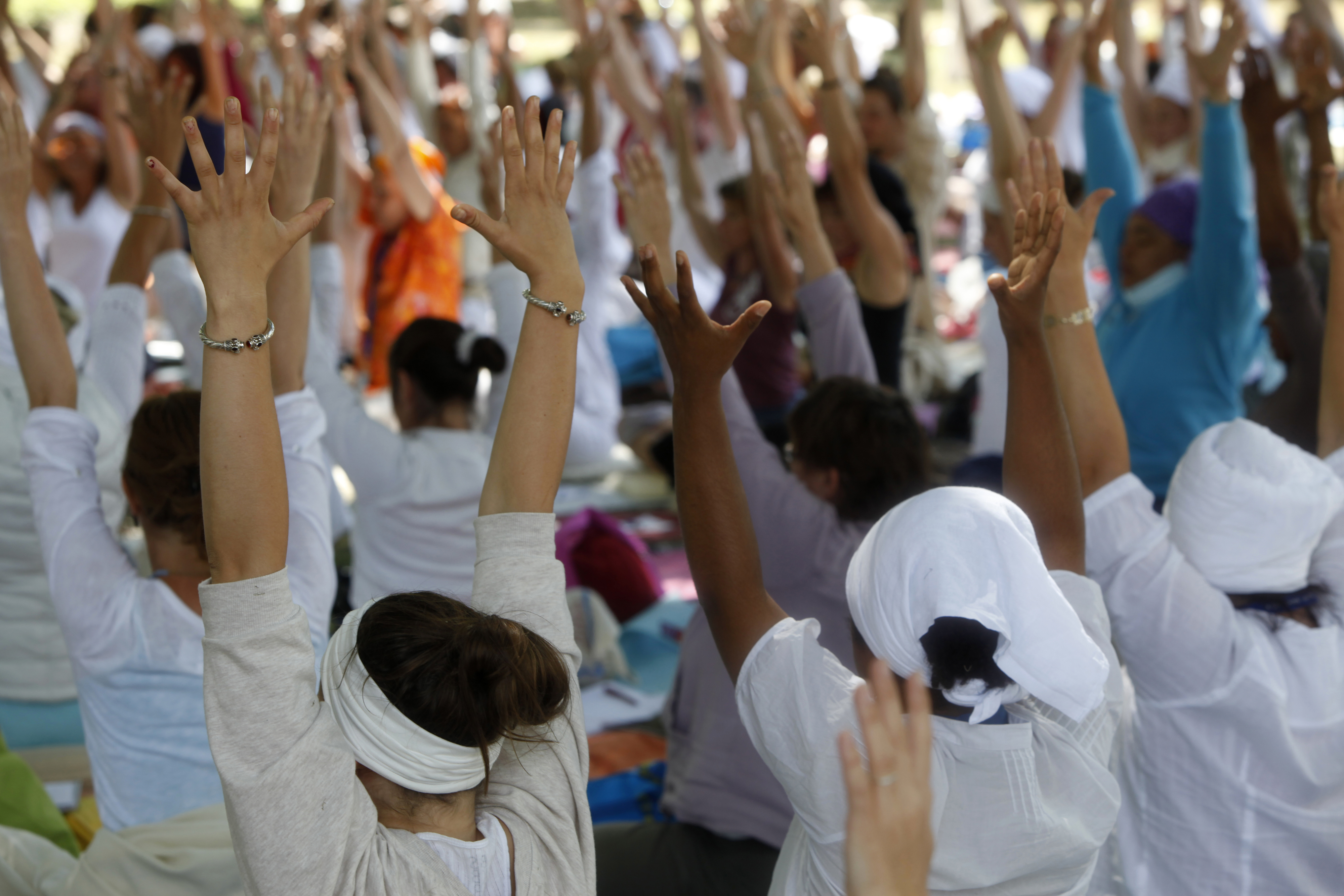 Group of people in white clothing with arms raised in a yoga pose, promoting wellness and community