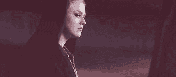 Person resembling Queen Ravenna with a chain necklace, focused expression, stylized dark attire