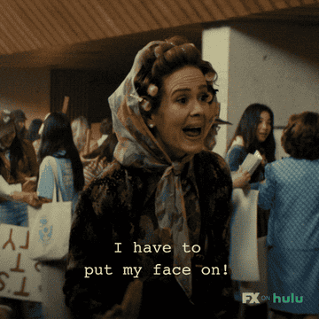 Sarah paulson in vintage attire with hair curlers gestures while saying &quot;i have to put my face on&quot;