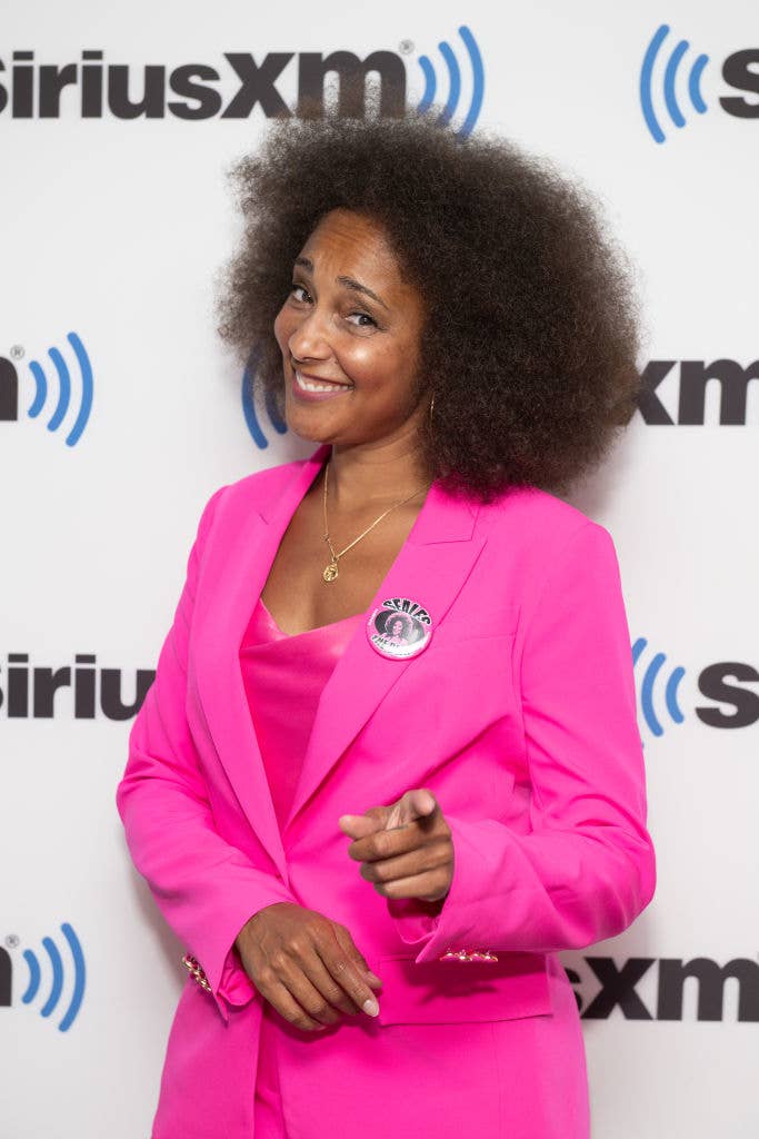Person wearing a pink blazer with a "SiriusXM" backdrop, smiling and posing