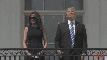 Donald and Melania Trump stand together on a balcony. Donald wears a suit and tie; Melania is in a sleeveless dress