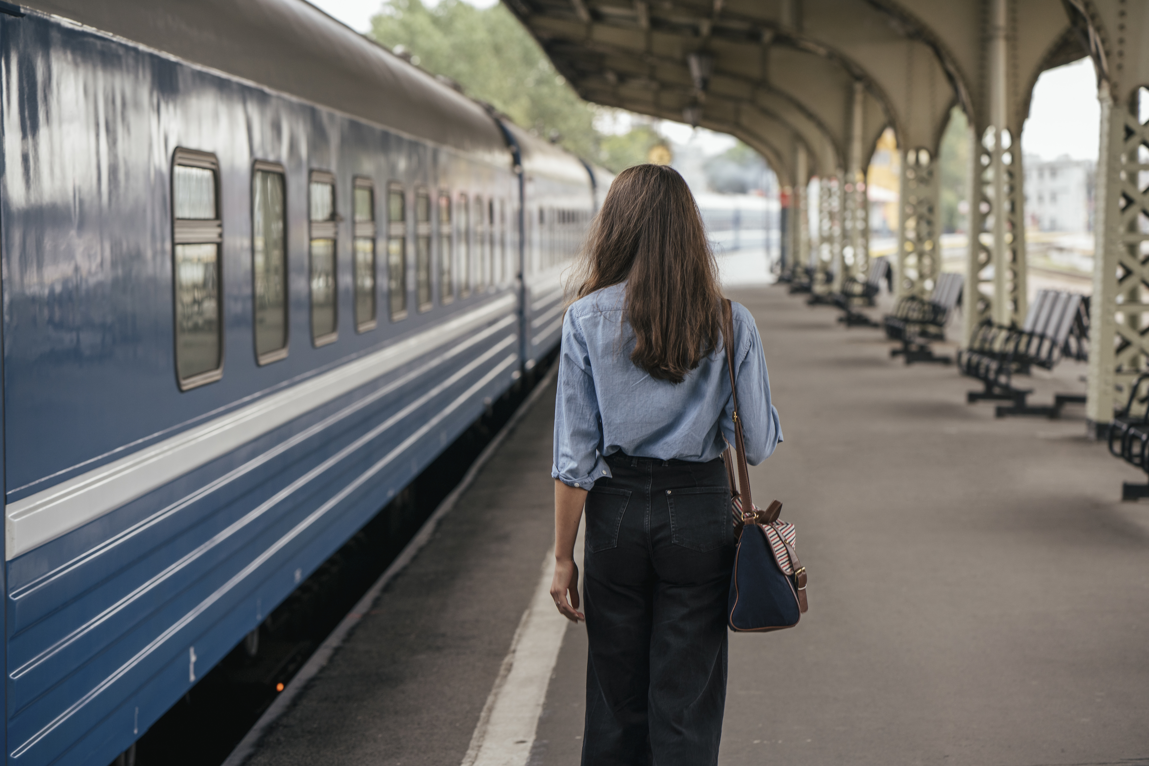 Woman standing on a train platform with her back to the camera, looking towards a train