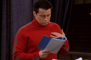 Man in red sweater looks confused at blue papers he's holding