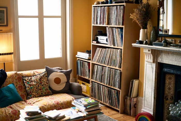 A cozy living room with bookshelves, a patterned couch, records, and a fireplace