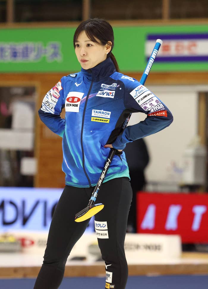 カーリング選手がコートに立ち、ブルーユニフォームを着てブラシを持っています。