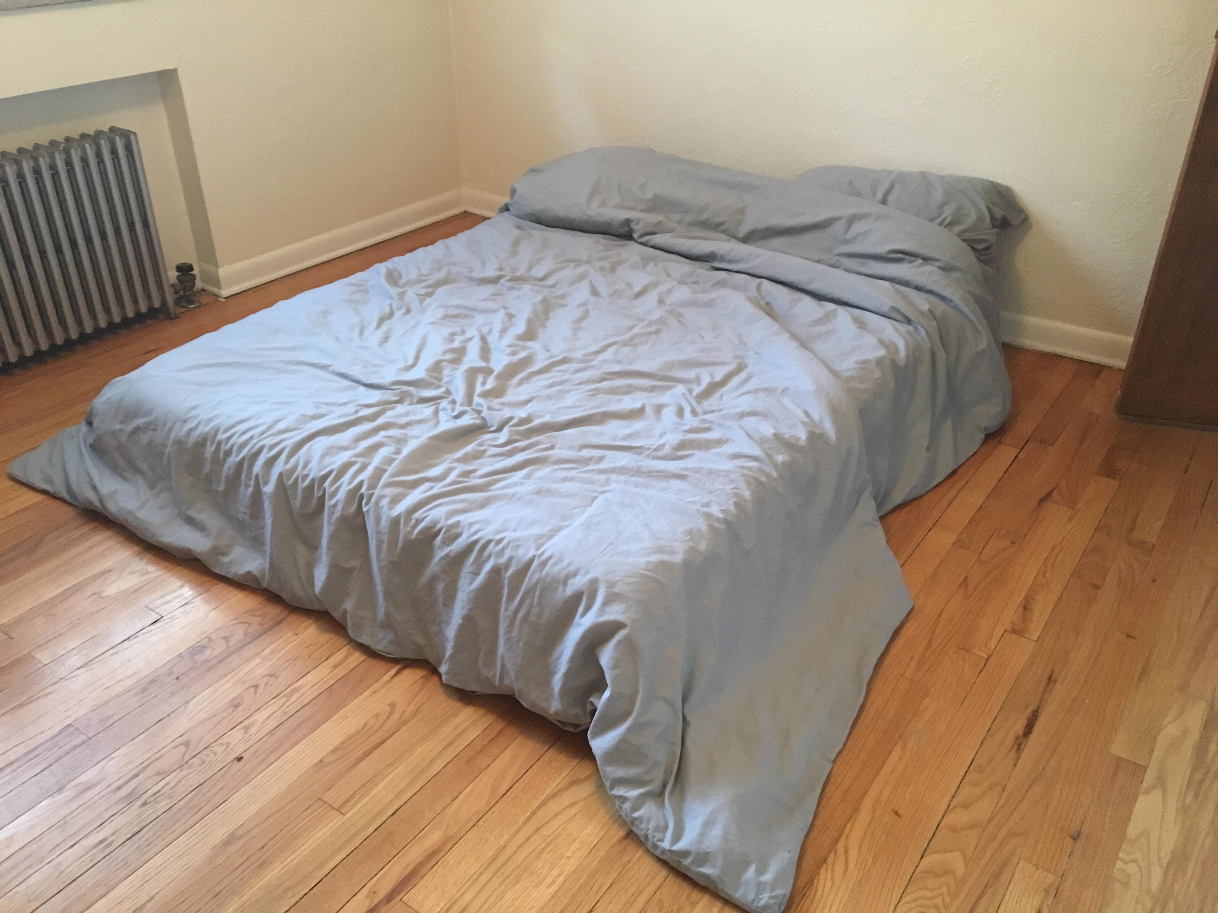 Unmade bed with a grey duvet on a wooden floor